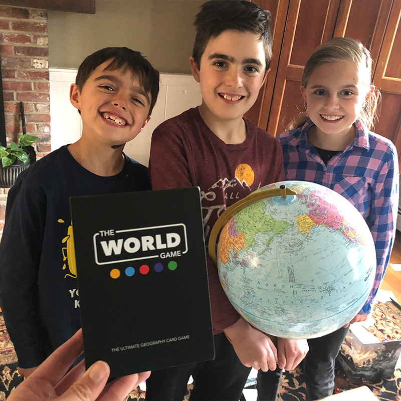 Children enjoying playing the world game card game with world globe in front learning about geography through homeschooling